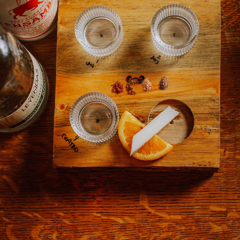 A flight of Mezcal shots served on a wood board.